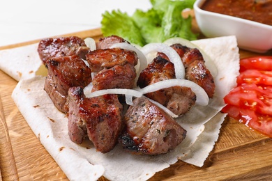 Photo of Wooden board with juicy shish kebab, closeup