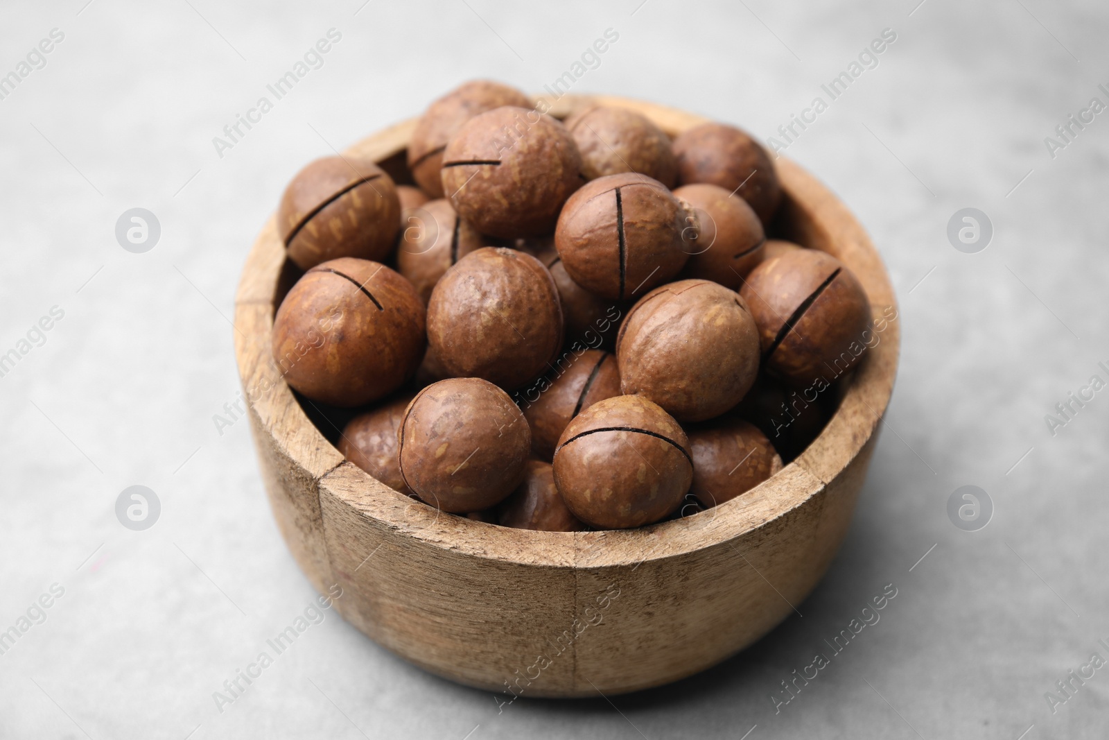 Photo of Delicious macadamia nuts in bowl on light grey table, closeup