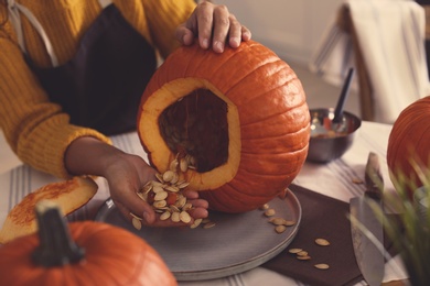 Photo of Woman making pumpkin jack o'lantern at table, closeup. Halloween celebration