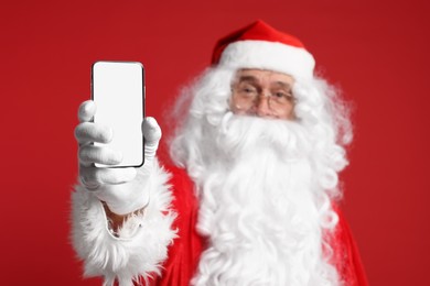 Photo of Merry Christmas. Santa Claus showing smartphone on red background, selective focus. Mockup for design