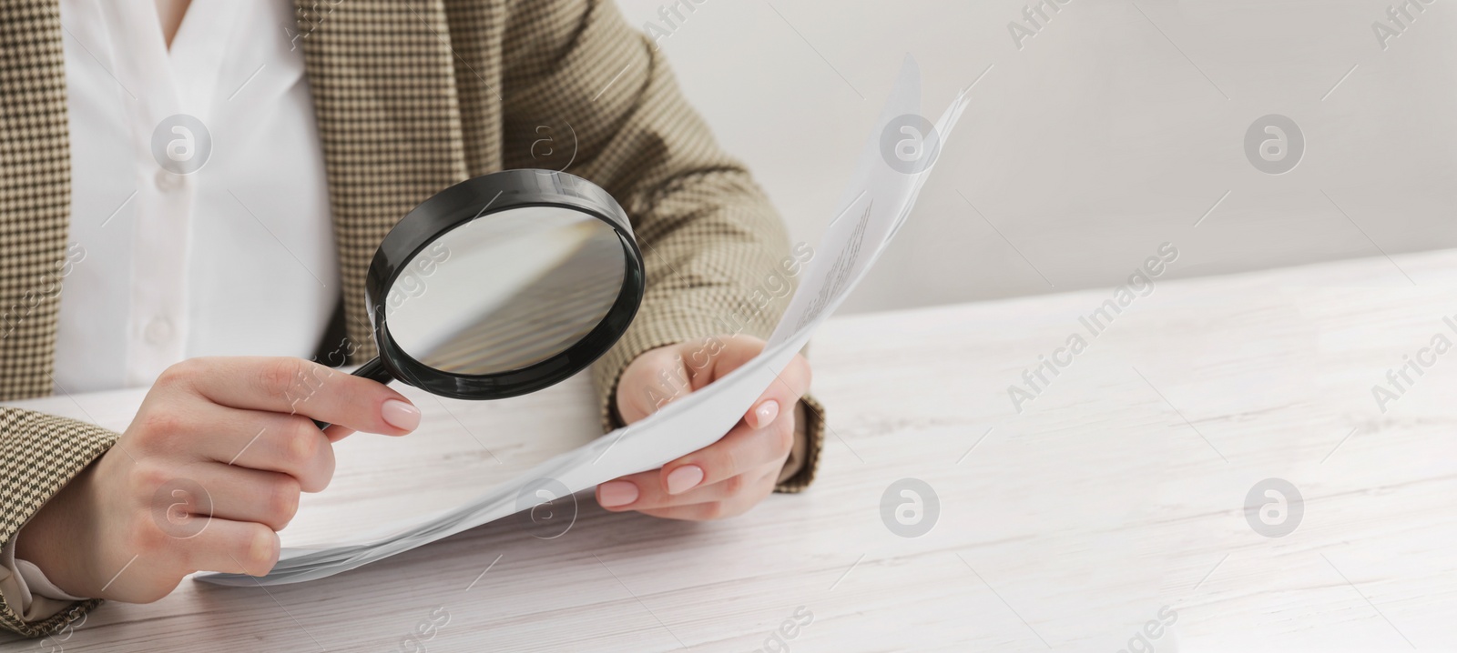 Image of Woman looking at documents through magnifier at white wooden table, closeup. Banner design with space for text