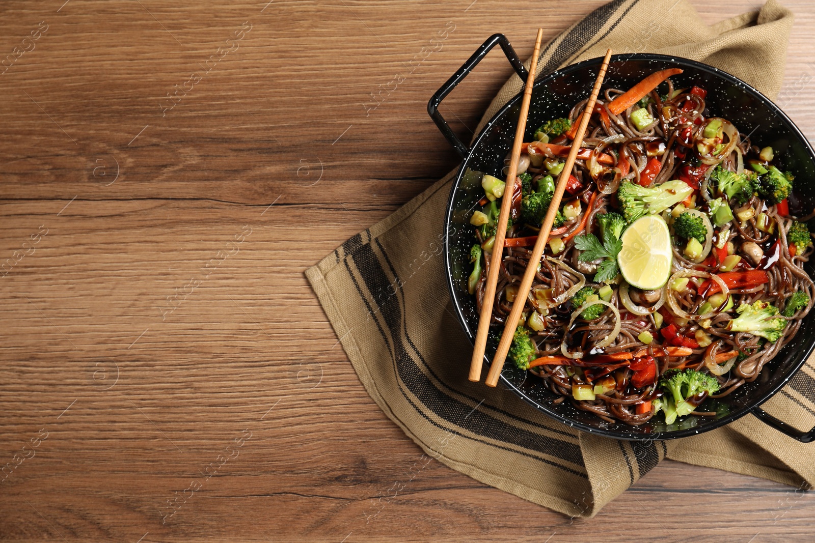 Photo of Stir-fry. Tasty noodles with meat in wok and chopsticks on wooden table, top view. Space for text