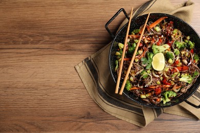 Photo of Stir-fry. Tasty noodles with meat in wok and chopsticks on wooden table, top view. Space for text