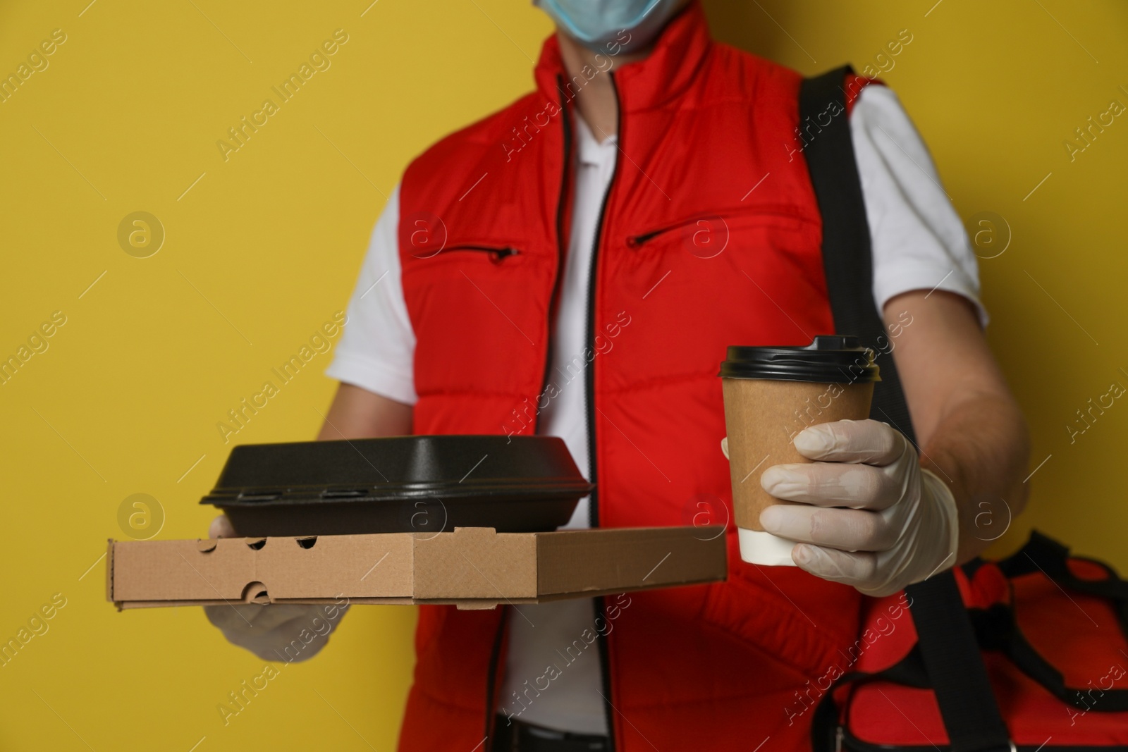 Photo of Courier in protective gloves holding order on yellow background, closeup. Food delivery service during coronavirus quarantine