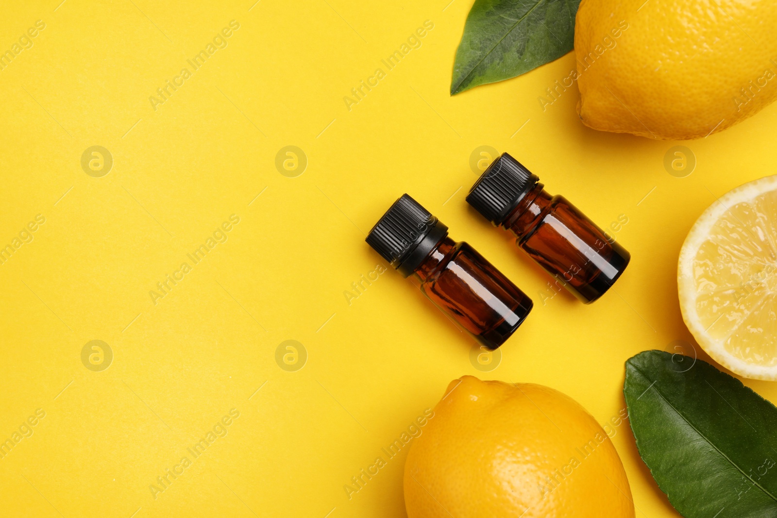 Photo of Bottles of citrus essential oil, fresh lemons and leaves on yellow background, flat lay. Space for text