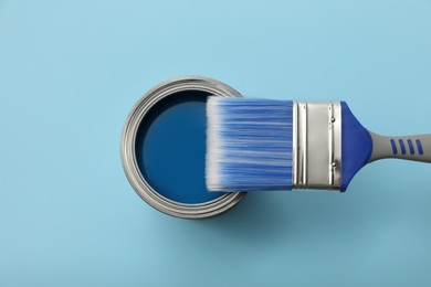 Photo of Can of paint and brush on light blue background, top view