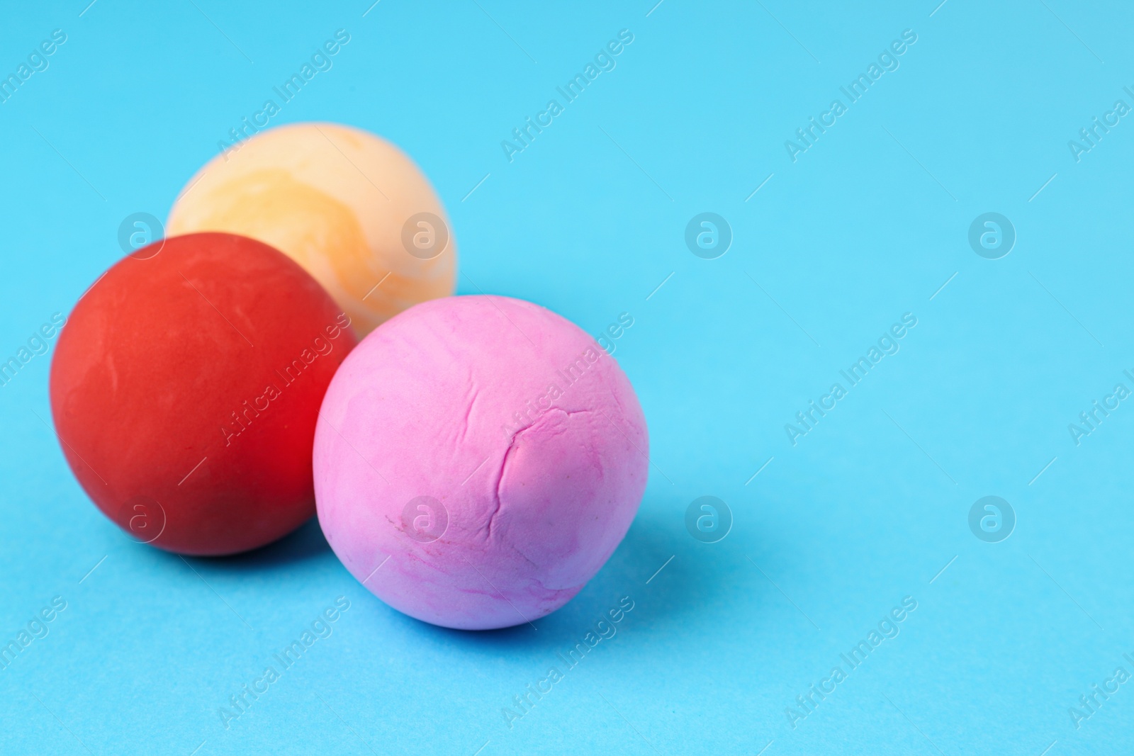 Photo of Different color play dough balls on light blue background, closeup. Space for text