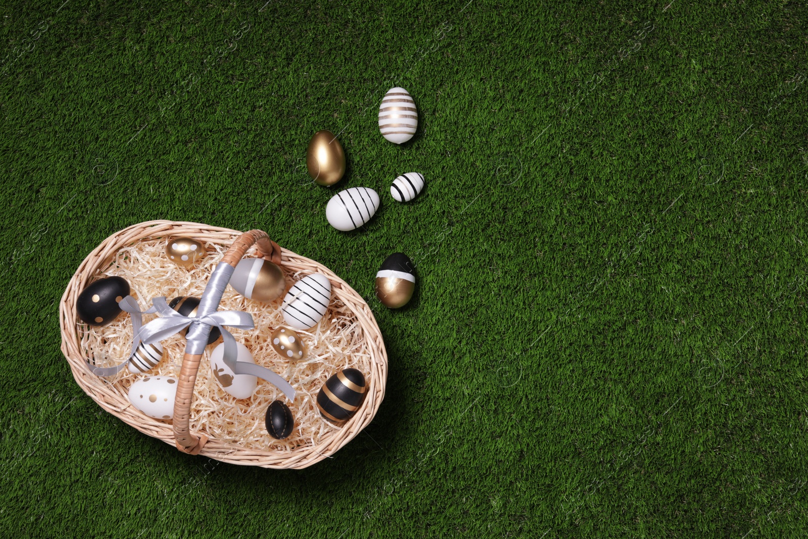 Photo of Easter basket and beautifully painted eggs on green grass, flat lay. Space for text