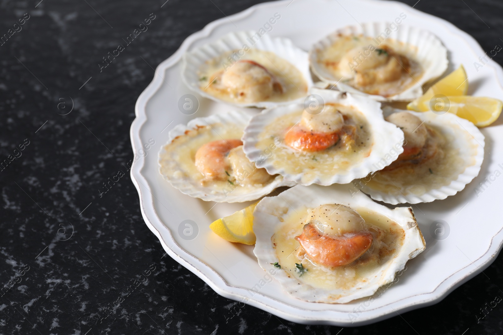 Photo of Fried scallops in shells and lemon on black textured table, closeup