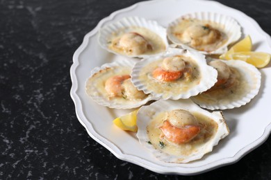 Photo of Fried scallops in shells and lemon on black textured table, closeup