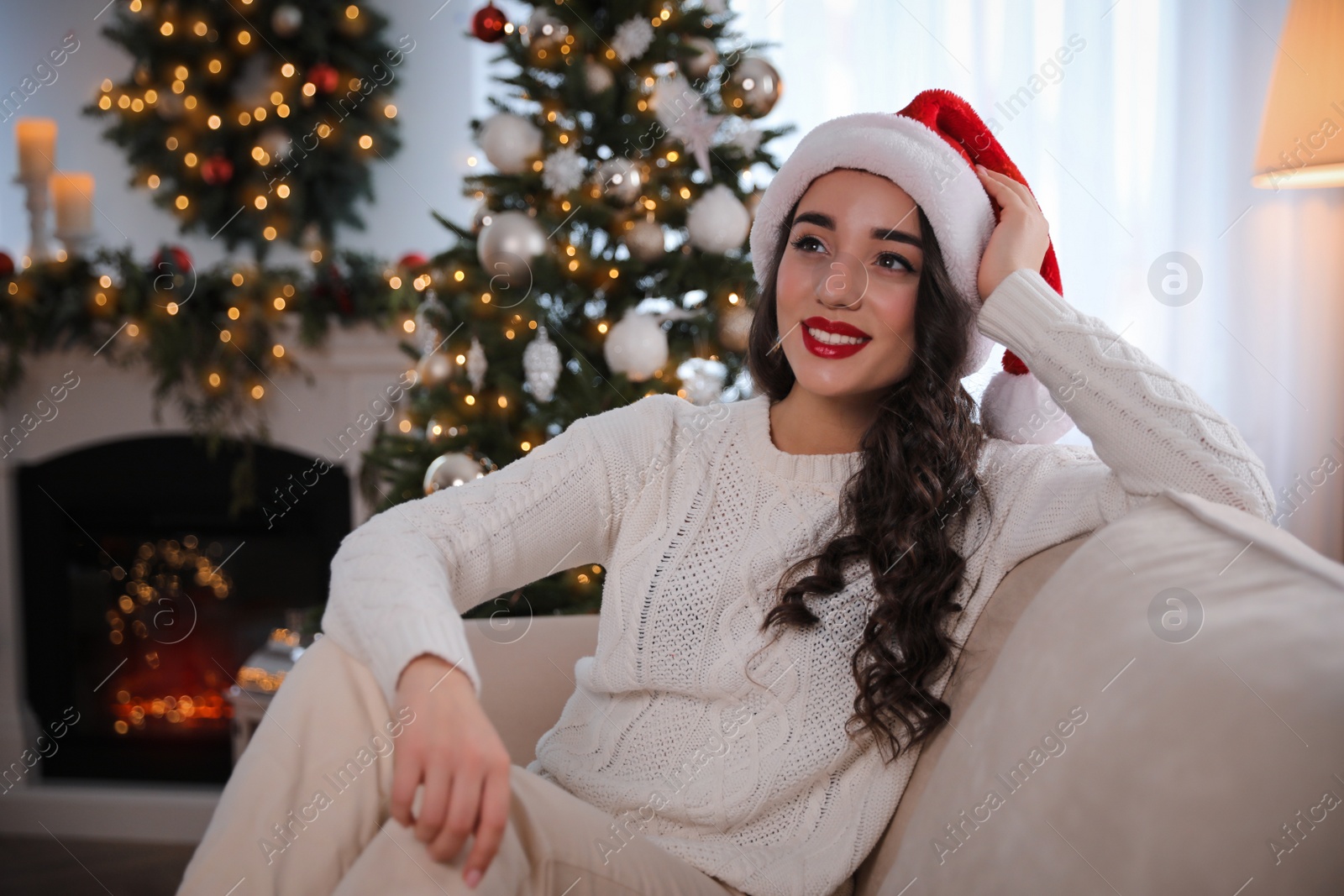 Photo of Beautiful young woman wearing Santa hat in room decorated for Christmas