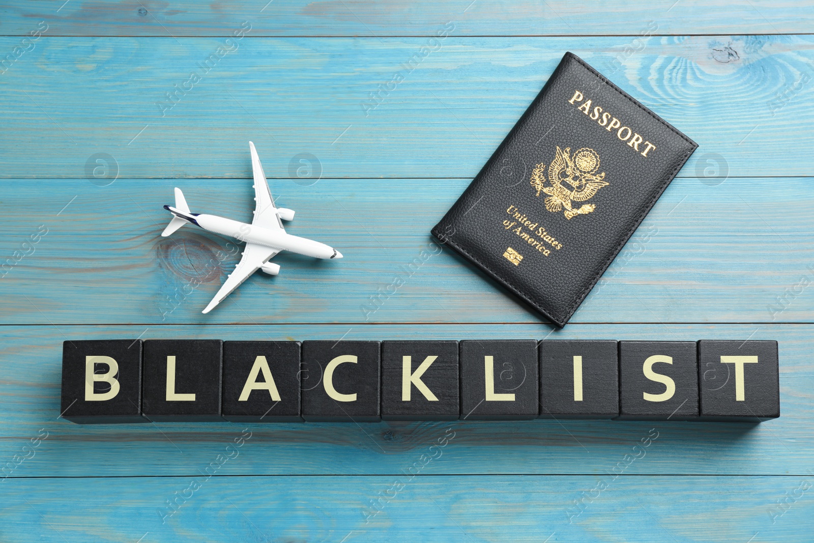 Photo of Black cubes with word Blacklist, toy airplane and passport on turquoise wooden background, flat lay