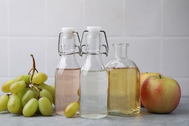 Photo of Different types of vinegar and fresh fruits on grey table