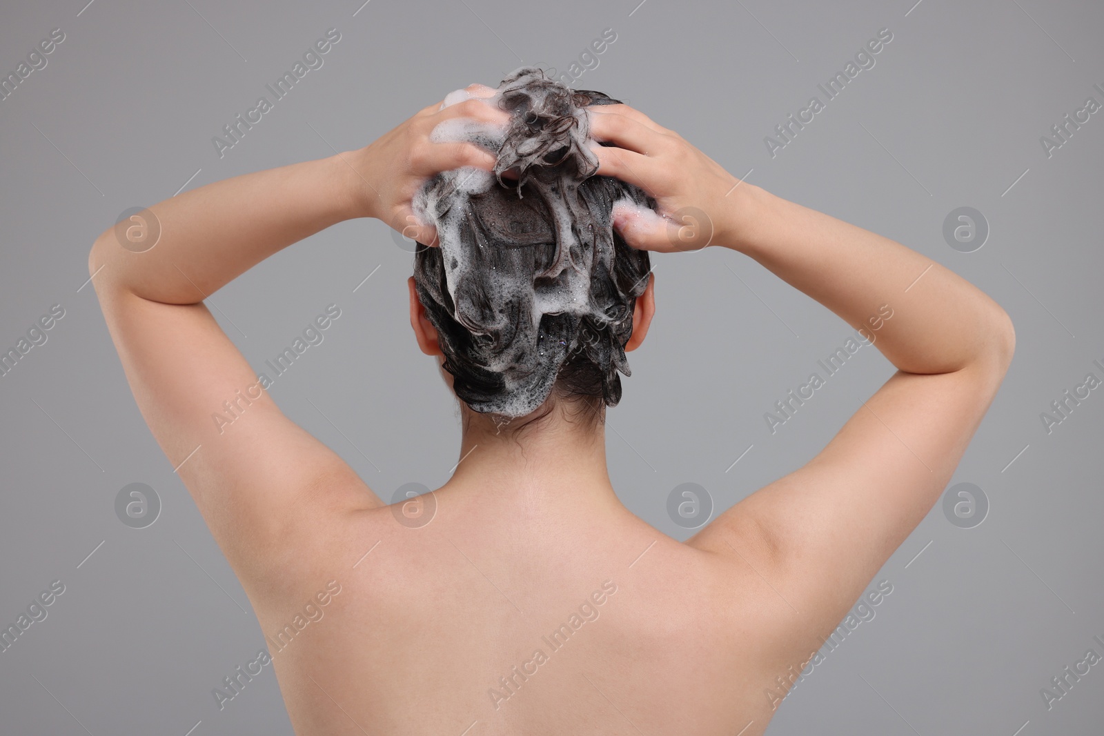 Photo of Woman washing hair on grey background, back view