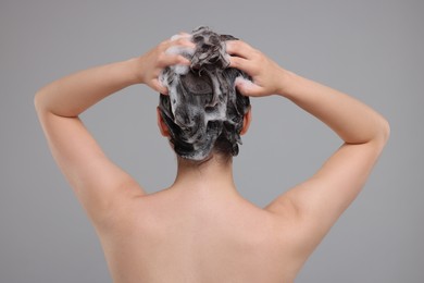 Photo of Woman washing hair on grey background, back view