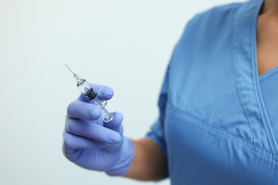 Doctor holding syringe with COVID-19 vaccine on light background, closeup