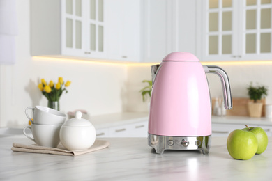 Photo of Modern electric kettle, tea set and apples on table in kitchen