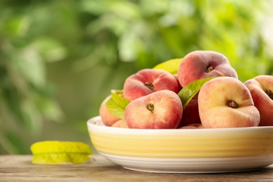 Photo of Fresh ripe donut peaches on wooden table against blurred green background, closeup. Space for text