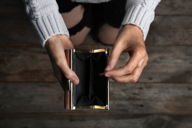 Poor woman holding empty wallet and coin on wooden background, closeup