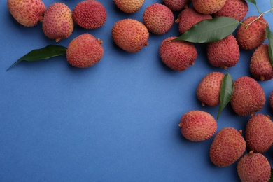 Photo of Fresh ripe lychees with leaves on blue background, flat lay. Space for text