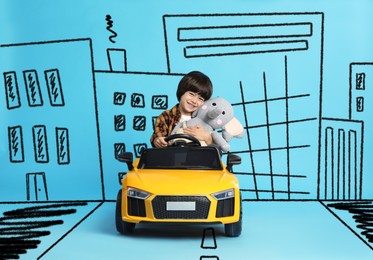 Cute little boy with toy driving car and drawing of city on light blue background