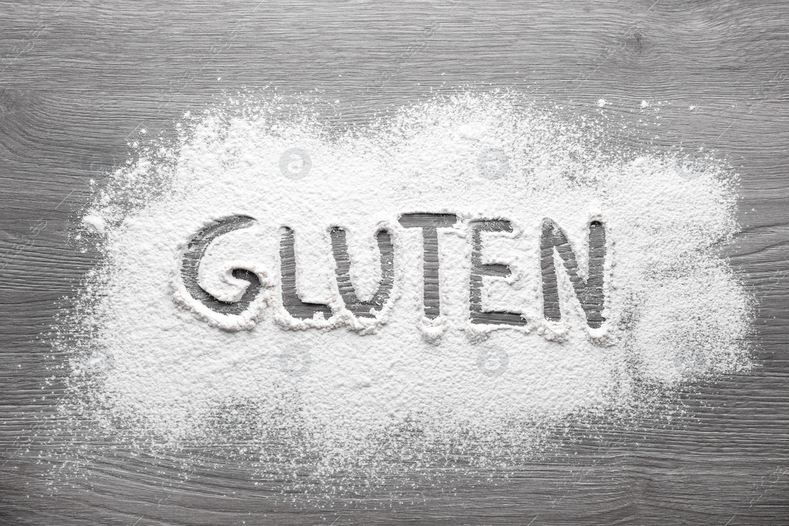 Photo of Word Gluten written with flour on wooden table, top view