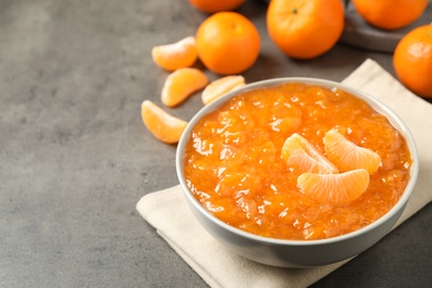 Photo of Tasty tangerine jam in bowl on grey table. Space for text