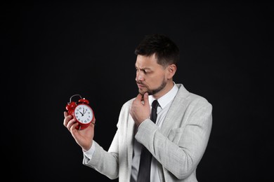 Photo of Businessman holding alarm clock on black background. Time management