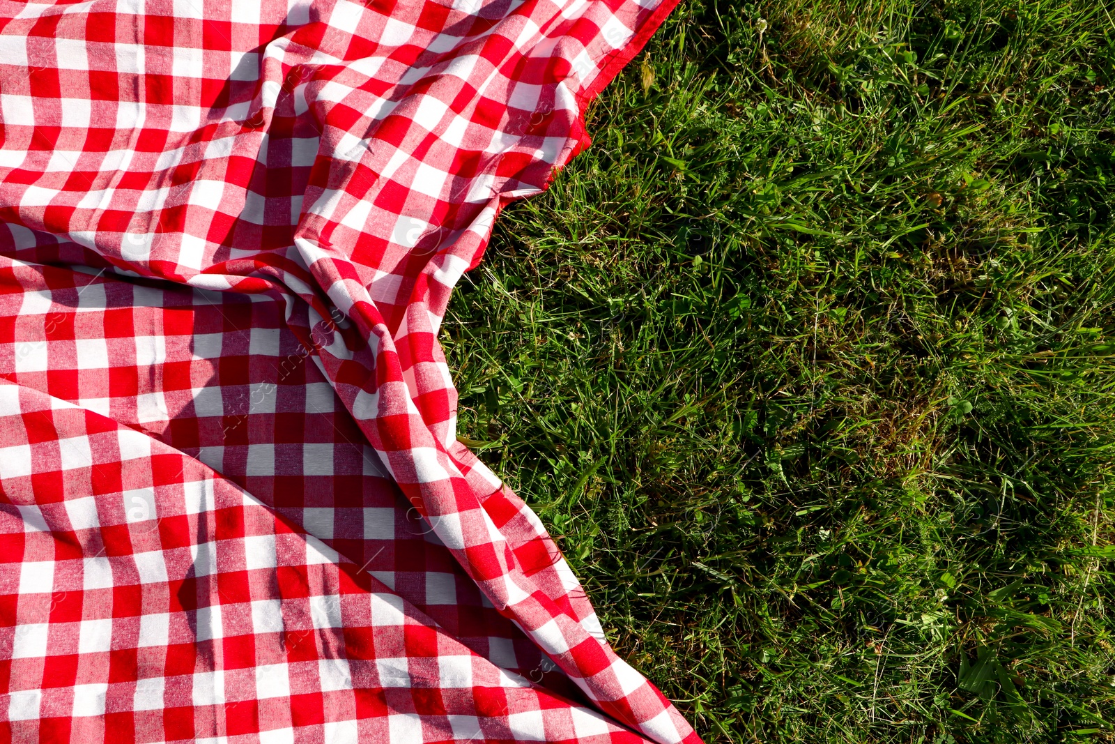 Photo of Checkered picnic tablecloth on fresh green grass, top view. Space for text