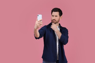 Man taking selfie with smartphone on pink background, space for text