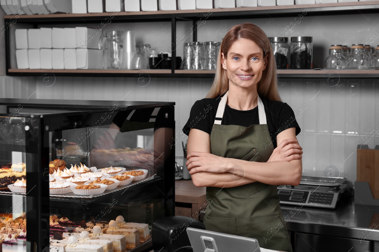 Photo of Happy seller near showcase with different delicious desserts in bakery shop