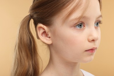 Photo of Little girl with hearing aid on pale brown background, closeup