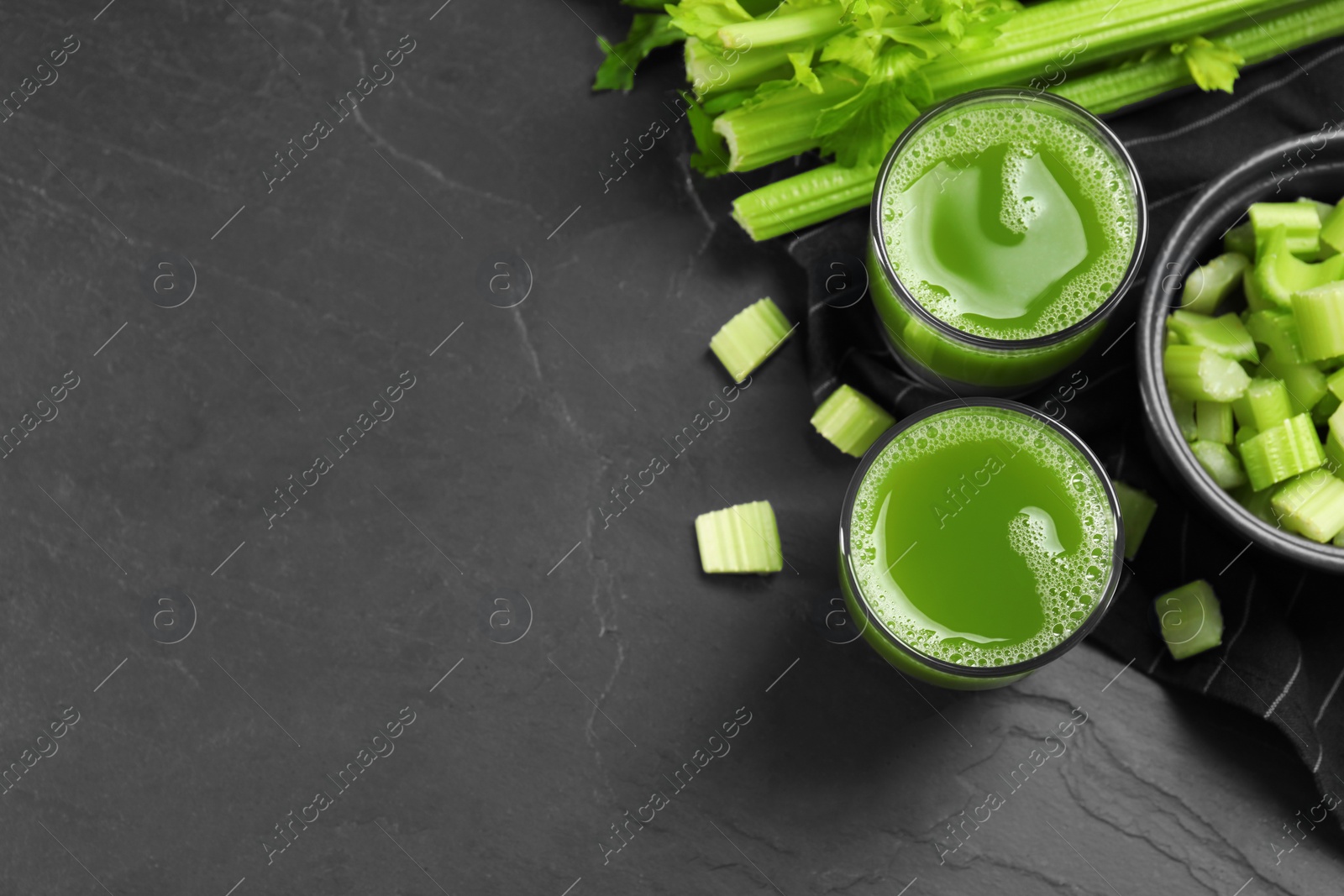 Photo of Glasses of delicious celery juice and vegetables on black table, flat lay. Space for text