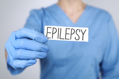 Photo of Doctor holding card with word Epilepsy on light grey background, closeup
