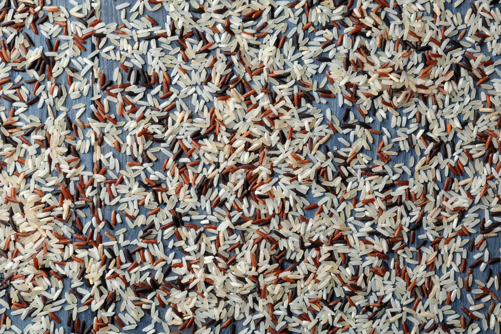 Photo of Brown and other types of rice scattered on color wooden background