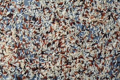 Photo of Brown and other types of rice scattered on color wooden background