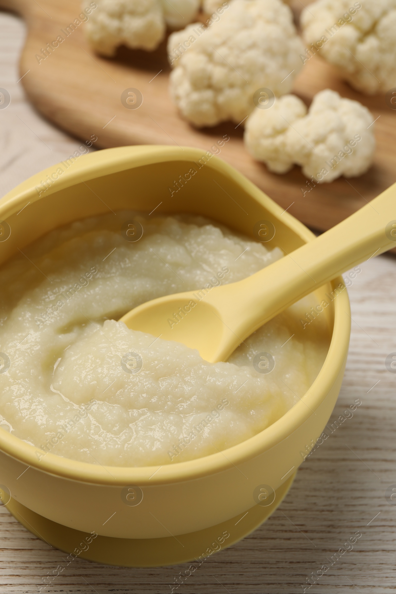 Photo of Baby food. Bowl with tasty cauliflower puree on light wooden table, closeup