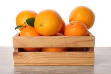 Fresh oranges in crate on light wooden table against white background