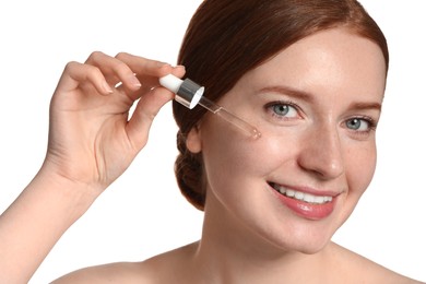 Photo of Smiling woman with freckles applying cosmetic serum onto her face on white background, closeup
