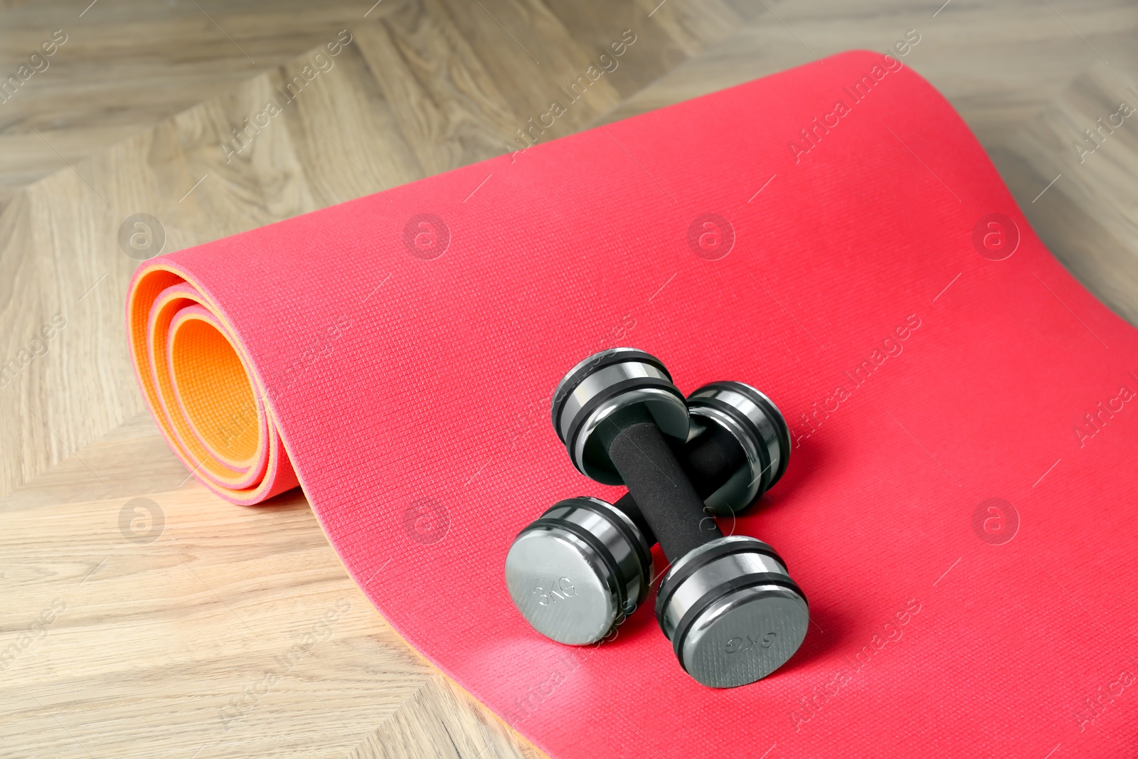 Photo of Exercise mat and dumbbells on wooden floor indoors