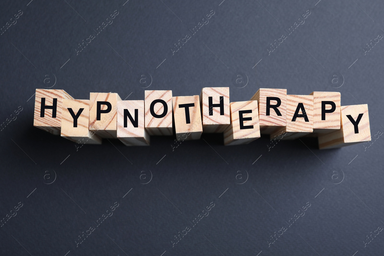 Photo of Wooden blocks with word HYPNOTHERAPY on black background, flat lay