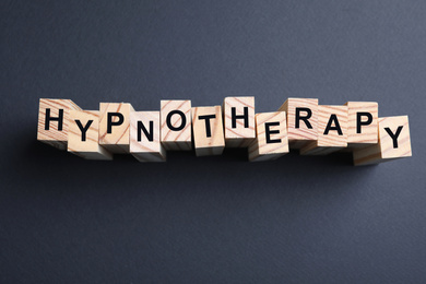 Wooden blocks with word HYPNOTHERAPY on black background, flat lay