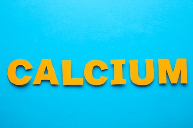 Photo of Word Calcium made of orange letters on light blue background, flat lay
