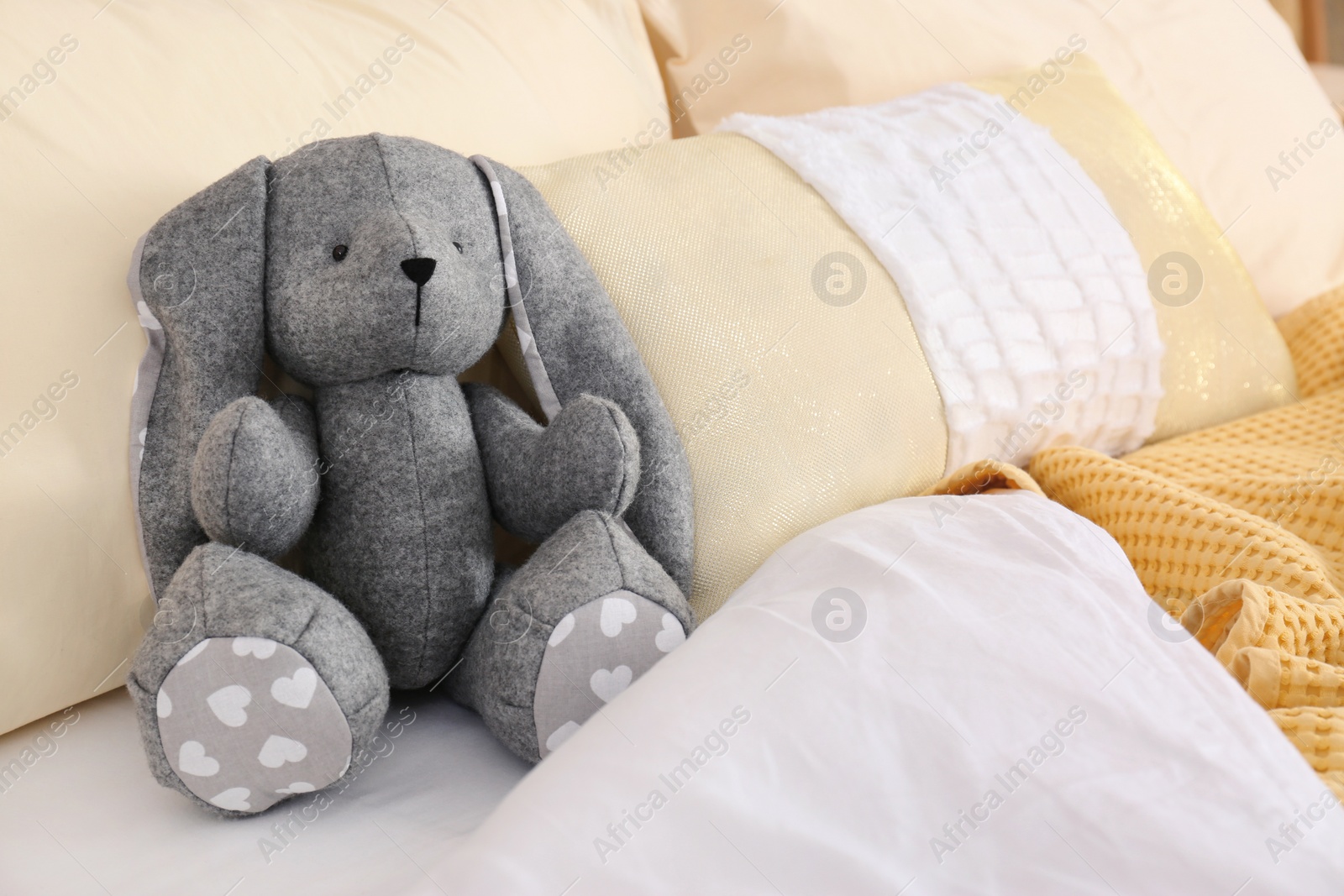 Photo of Cute toy rabbit on bed in child's room interior. Space for text