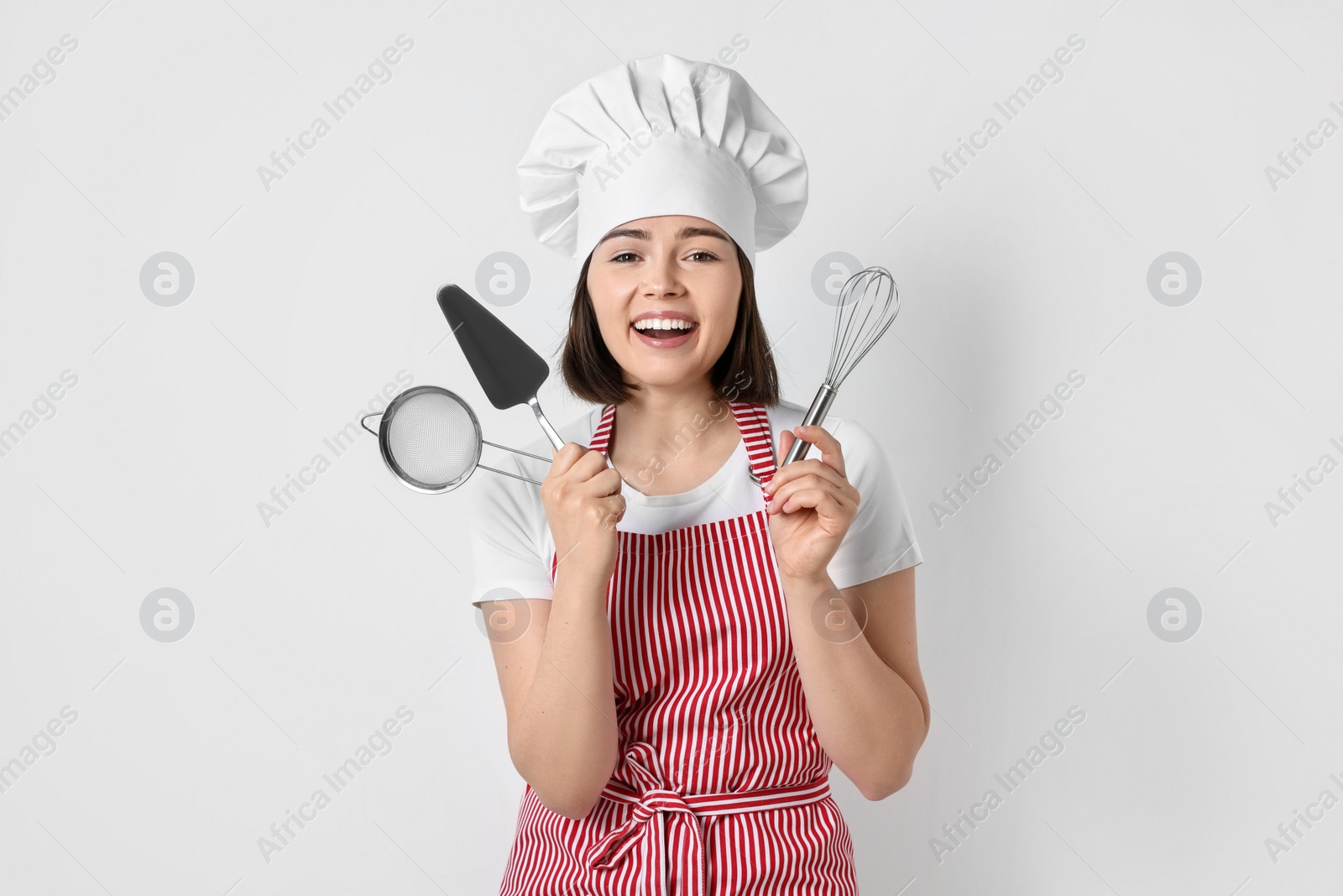 Photo of Happy confectioner holding professional tools on light grey background