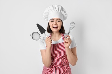 Happy confectioner holding professional tools on light grey background