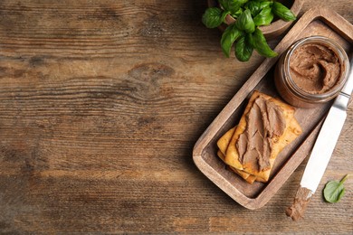 Crispy crackers with delicious meat pate and knife on wooden table, flat lay. Space for text