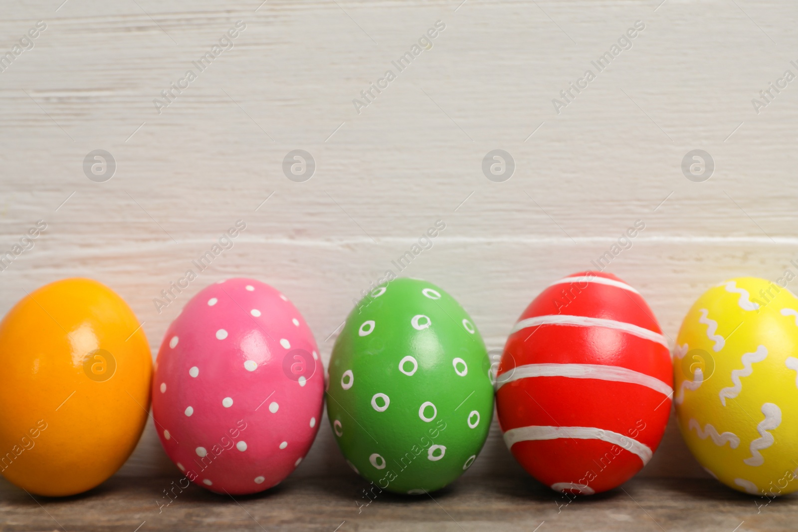 Photo of Decorated Easter eggs on table near wooden wall. Space for text