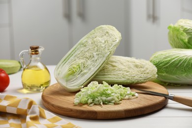 Photo of Fresh Chinese cabbages, knife and oil on white wooden table in kitchen