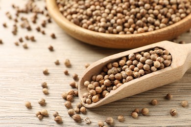 Photo of Dried coriander seeds in bowl and scoop on wooden table, closeup